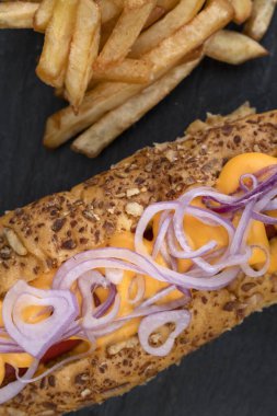 Kırmızı soğanlı sosisli, çedar peyniri ve siyah tabakta patates kızartması..