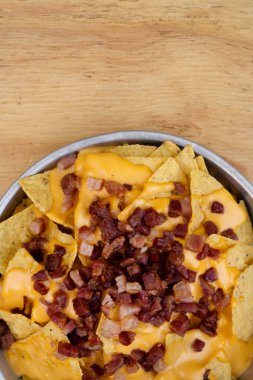 Çedar arkaplanlı cips. Çedar peynirli cips ve ahşap masadaki metal tabakta gevrek domuz pastırması..