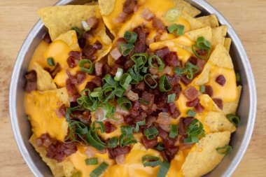 Çedar arkaplanlı cips. Çedar peynirli nachos, yeşil soğan ve ahşap bir tabakta gevrek domuz pastırması..