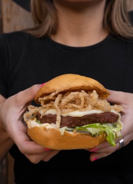 Bitki bazlı burger. Burger değil. Elinde marul, çıtır soğan halkası, peynir ve NotCo mayonezli Notco hamburgeri olan bir kadının yakın görüntüsü..