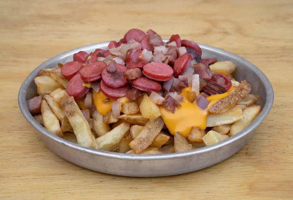 Stock image Fries. Closeup view of fried potatoes with sliced sausages and crispy bacon, in a metal dish with a wooden background.