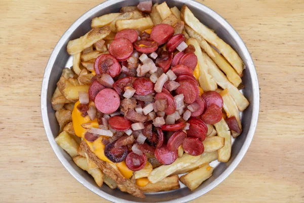 stock image Fries. Top view of fried potatoes with sliced sausages and crispy bacon, in a metal dish with a wooden background.