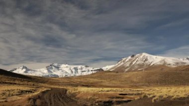 Altın çayır ve dağların arasından toprak yol boyunca seyahat ediyor. Ufukta Volkan Domuyo 'ya giden yolun görüntüsü.