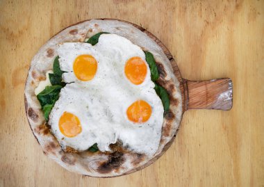 Ahşap masada peynirli, ıspanaklı ve sahanda yumurtalı bir pizzanın en üst görüntüsü..