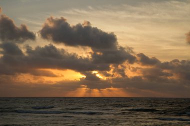 Dramatik sahil manzarası. Deniz ve okyanus dalgaları üzerinde turuncu güneş ışınları ve bulutlarla güzel gün batımı gökyüzü. 