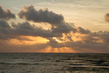 Dramatik sahil manzarası. Turuncu güneş ışınları ve bulutlarla güzel gün batımı gökyüzü, deniz üzerinde ve alacakaranlıkta okyanus dalgaları. 