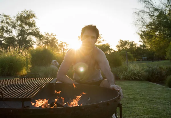 Lifestyle and cooking outdoor. Barbecue. Portrait of a young caucasian attractive man besides the campfire, ready for grilling in the garden at sunset.