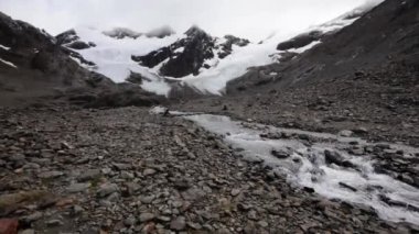 Alp manzarası. Buzul su akıntısı kayalık dağ boyunca akıyor. Arjantin, Tierra del Fuego 'daki Buzul Vinciguerra' nın eriyen su akımının yavaş çekim görüntüsü..