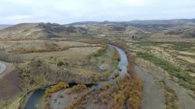 Vadiden ve dağlardan akan nehrin havadan görünüşü. Toprak yol manzarası, sarı çayır, tepeler ve Patagonya 'daki kayalık uçurum..