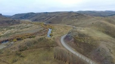 Vadiden ve dağlardan akan nehrin havadan görünüşü. Toprak yol manzarası, sarı çayır, tepeler ve Patagonya 'daki kayalık uçurum..