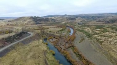 Vadiden ve dağlardan akan nehrin havadan görünüşü. Toprak yol manzarası, sarı çayır, tepeler ve Patagonya 'daki kayalık uçurum..