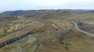 Vadiden ve dağlardan akan nehrin havadan görünüşü. Toprak yol manzarası, sarı çayır, tepeler ve Patagonya 'daki kayalık uçurum..