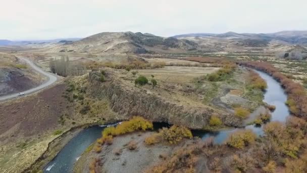 从空中俯瞰流过山谷和群山的河流 巴塔哥尼亚的土路 黄色的草地 山丘和岩石悬崖 — 图库视频影像