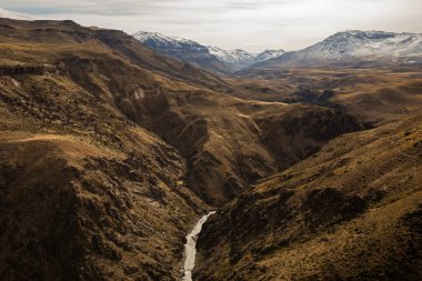 Altın vadi. Sarı çayır ve dağların arasından akan kayalıkların ve derenin manzarası. Volkan Domuyo arka planda. 