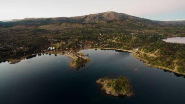 Turizm. Gün batımında göl. Sakin köyün havadan görünüşü. Koyun, limanın, adanın, ormanın ve dağların üzerine..