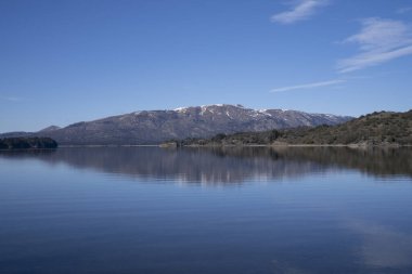 Güneşli bir sabahta göl. Ormanın manzarası, göl ve mavi sudaki gökyüzünün mükemmel yansıması. Arka planda And Dağları sıradağları.