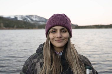 Gülümseyen genç bir kadının portresi. Arka planda durgun göl ve sıradağlar var. Çevrede güzel günbatımı renkleri.