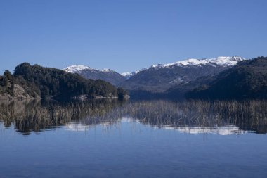 Alplerde yaz günü. Göl yüzeyindeki mavi gökyüzünün, yeşil ormanın ve dağların yansıması..