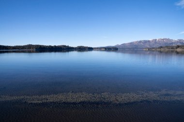Güneşli bir sabahta göl. Ormanın manzarası, göl ve mavi sudaki gökyüzünün mükemmel yansıması. Arka planda And Dağları sıradağları.