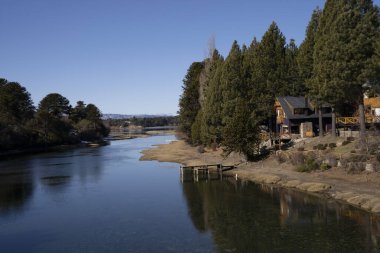Ormanda bir kulübe. Güneşli bir yaz gününde ormanın sakin gölü ve ahşap evi manzarası. Su yüzeyinde güzel bir çevre yansıması. 