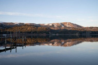 Gün batımında huzurlu göldeki ahşap iskelede. Orman ve And Dağları arka planda. Ormanın, dağların ve sudaki alacakaranlık gökyüzünün güzel yansıması. 