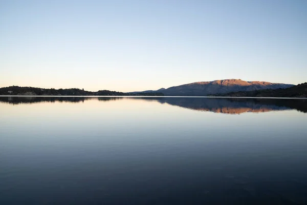 stock image Enchanting view of the placid lake at sunset. The mountains, forest and blue sky reflection in the water. 