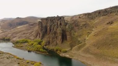 Altın vadi ve tepeler boyunca akan nehrin havadan görünüşü. Patagonya 'daki sarı çayır ve kaya oluşumlarının görüntüsü.