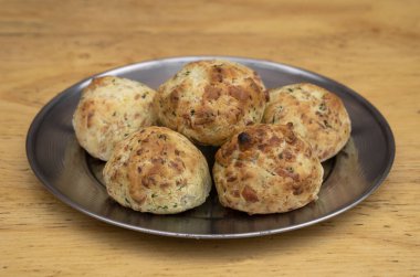 Küçük, fırınlanmış, peynir aromalı ruloların yakın görüntüsü, chipa olarak adlandırılır, ahşap arka planda metal bir çanakta.