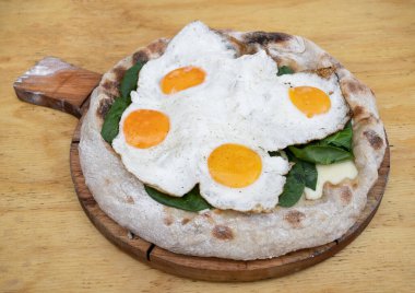 Ahşap masada mozzarella peynirli, ıspanaklı ve sahanda yumurtalı bir pizzanın yakın görüntüsü.. 