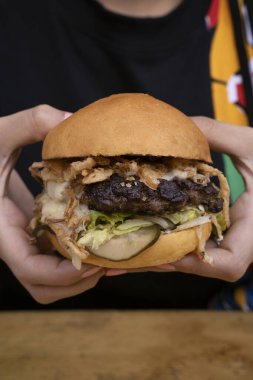 Canavar burger. Elinde mozzarella peyniri, et, salatalık turşusu, mayonez, marul ve kızarmış soğanlı çoklu katmanlı hamburger tutan kadın..