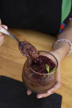 Tatlı yiyorum. Yakından bakınca elinde kaşıkla kırmızı böğürtlen soslu çikolatalı puding yiyen bir kadının resmi..