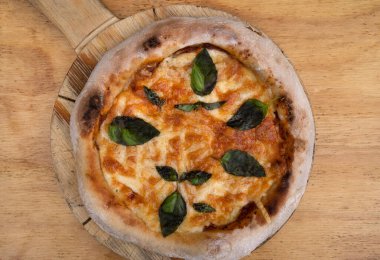 Geleneksel Margherita pizzası. Mozzarella ve parmesan peynirli, domates soslu ve fesleğenli bir pizzanın ahşap masanın üstünde üst görüntüsü..