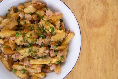 Amerikan yemeği. Restoranın ahşap masasındaki beyaz kasede yumurtalı, jambonlu, bezelyeli ve peynirli kızarmış patates manzarası..