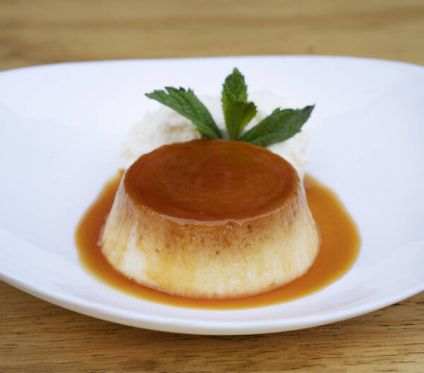 Традиционный десерт для гурманов. Крупный план пирога со сливками и карамелью, в белом блюде на деревянном столе.