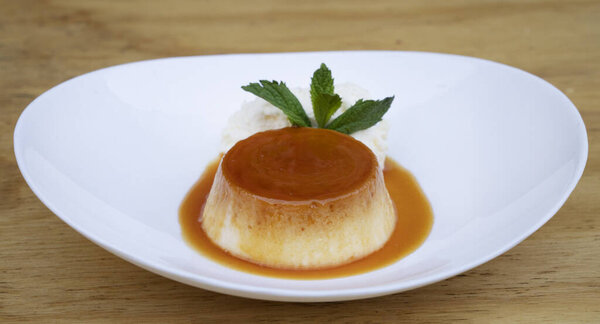 Традиционный десерт для гурманов. Крупный план пирога со сливками и карамелью, в белом блюде на деревянном столе.