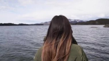 Tatiller. Yakından bakınca, kahverengi saçlı genç bir kadın sakin gölü ve ufuktaki dağları düşünüyor..