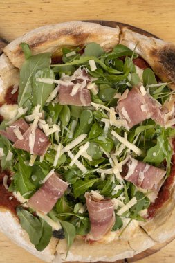 Arugula soslu pizza, jambon, parmesan peyniri, mozzarella peyniri ve domates sosu, ahşap masada.. 