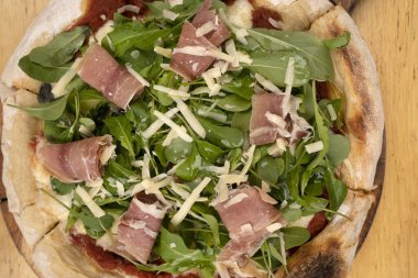 Arugula soslu pizza, jambon, parmesan peyniri, mozzarella peyniri ve domates sosu, ahşap masada.. 