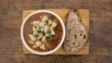 Geleneksel Macar yemeğinin üst görüntüsü, dana eti ve gnocchi ile gulaş güveci, ve bir somun ekmek, ahşap masa üzerinde..