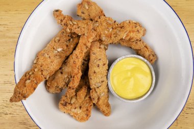 Tahta masadaki beyaz kasede körili mayonez soslu kızarmış tavuk parmakları manzarası..