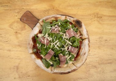 Arugula soslu pizza, jambon, parmesan peyniri, mozzarella peyniri ve domates sosu, ahşap masada..