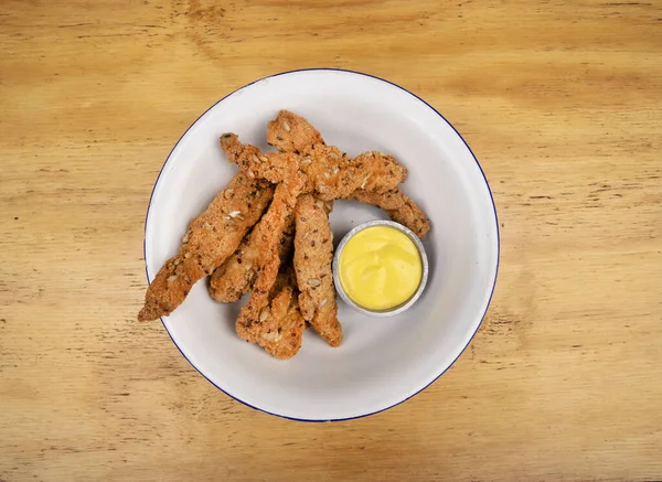 Tahta masadaki beyaz kasede körili mayonez soslu kızarmış tavuk parmakları manzarası..