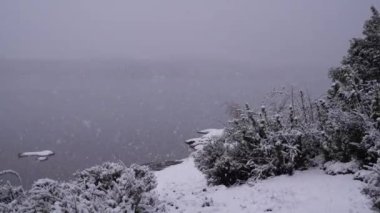 Kar yağıyor. Sabahın erken saatlerinde gölün, ormanın ve dağların üzerine düşen kar tanelerinin yavaş çekim görüntüsü..