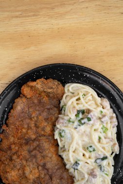 Makarna ve et. Milanesa 'nın en iyi manzarası, ekmek arası biftek, ve domuz pastırması ve pırasa kremalı spagetti, restoranın ahşap masasında siyah bir tabakta..