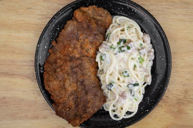 Makarna ve et. Milanesa 'nın en iyi manzarası, ekmek arası biftek, ve domuz pastırması ve pırasa kremalı spagetti, restoranın ahşap masasında siyah bir tabakta..