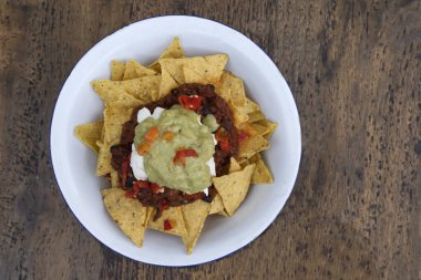 Meksika yemeği. Beyaz kasenin üst görüntüsü nachos, siyah fasulye saf, krem peynir ve guacamole, ahşap masa üzerinde.