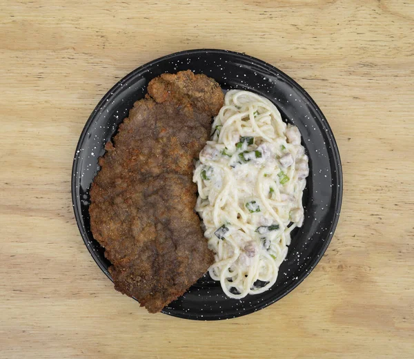 Makarna ve et. Milanesa 'nın en iyi manzarası, ekmek arası biftek, ve domuz pastırması ve pırasa kremalı spagetti, restoranın ahşap masasında siyah bir tabakta..