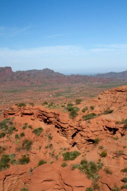 Dik kanyon. Kızıl çöl manzarası, uçurumlar, turuncu kumtaşı oluşumları ve ufuktaki kayalık dağlar.