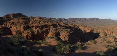Kırmızı kanyon. Kurak çöl manzarası, kumtaşı ve kayalık uçurumlar ve bulutlu mavi gökyüzünün altındaki dağlar..