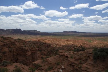 Kırmızı kanyon. Kurak çöl manzarası, kumtaşı ve kayalık uçurumlar ve bulutlu mavi gökyüzünün altındaki dağlar..